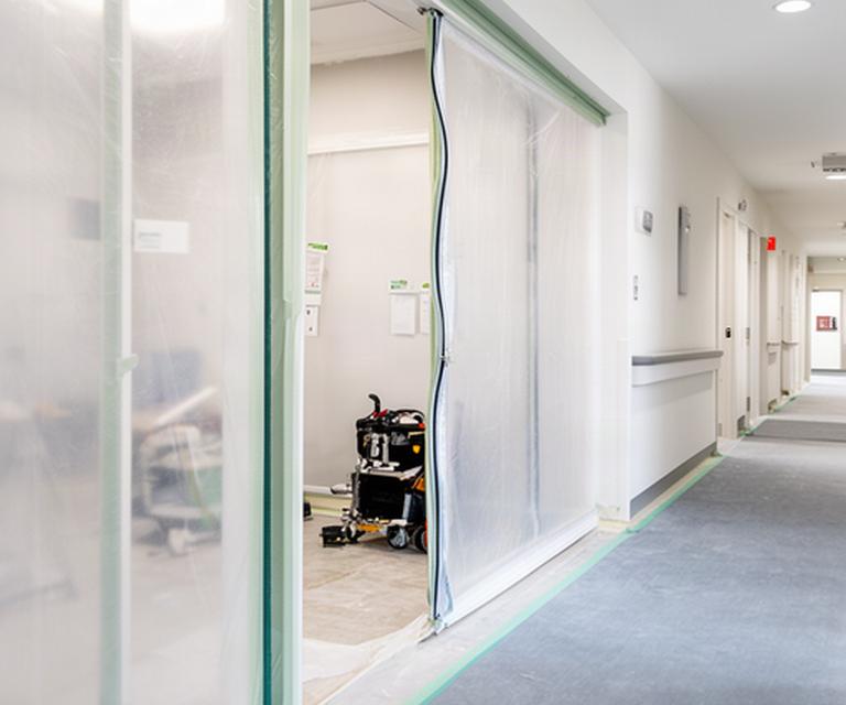 Clinic renovation work zone separated from an active corridor by sealed dust-control barriers and clearly managed access