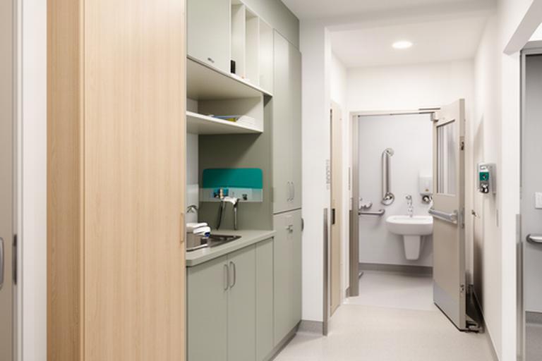 Clinic staff support area beside an accessible washroom, with organized storage, durable finishes and a clear corridor